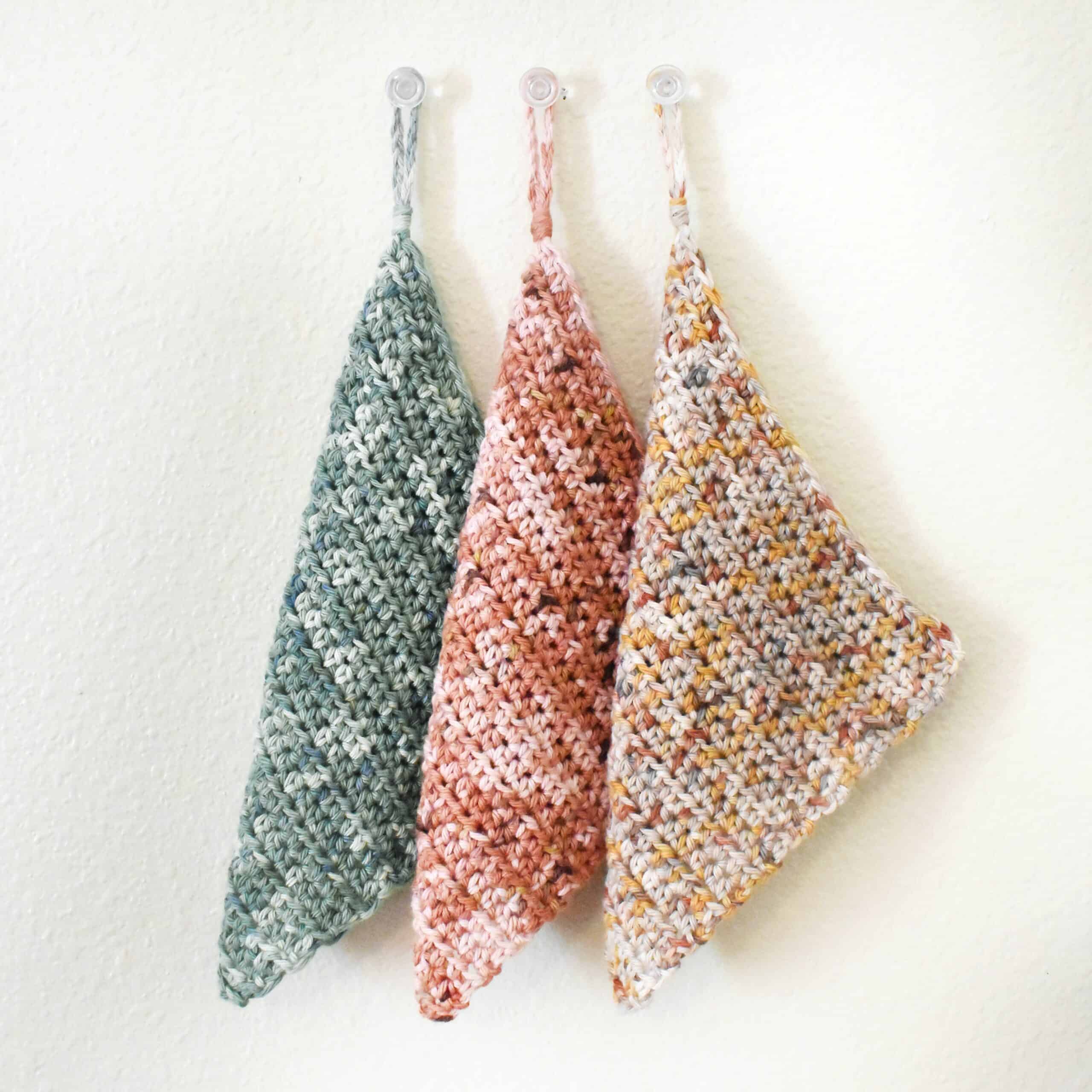 three pieces of crochet potholders hanging from hooks