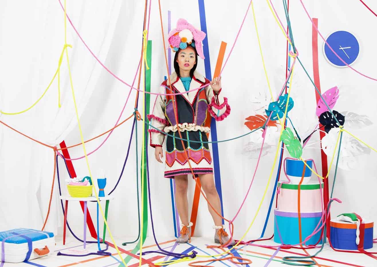 An Asian model stands in a colorful ribbon room wearing a colorful crochet dress by designer Katie Jones.