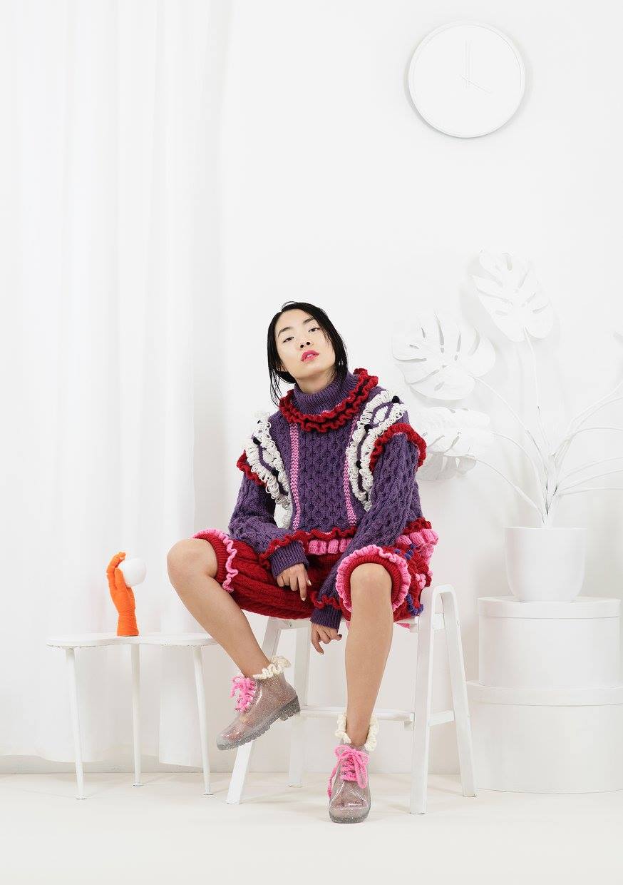 an Asian girl sits in knitted crochet purple-red-pink clothes from designer Katie Jones